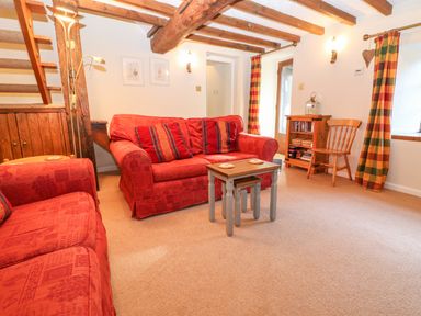 A living room with red sofas a small wooden table wooden beams on ceiling and checked curtains at Spring Cottage in Wroxton