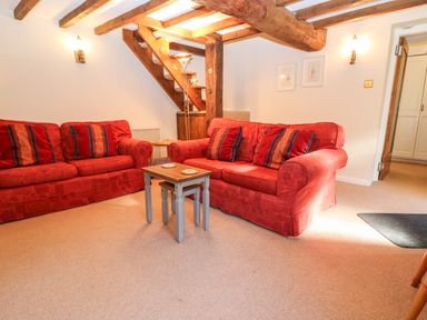 A sitting room with two red sofas and wooden stairs at Spring Cottage in Wroxton