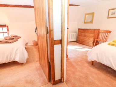 Two bedrooms separated by a wooden door with beds towels wooden chest of drawers chair and small window at Spring Cottage in Wroxton