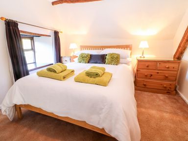 A bedroom with a wooden bed two bedside tables with lamps and a wooden dresser at Spring Cottage in Wroxton