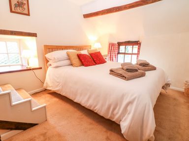 A bedroom with a double bed with white bedding and brown towels on it with two windows and carpet flooring at Spring Cottage in Wroxton