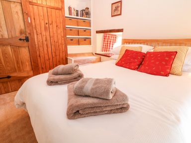 A bedroom with a wooden bed and red and beige cushions and folded towels on the bed at Spring Cottage in Wroxton