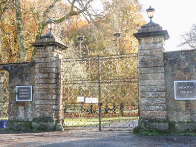 An iron gated entrance with stone pillars and lamps with signs for Fairleigh Dickinson University and Wroxton College in Wroxton