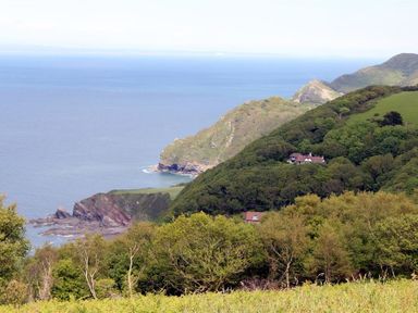 A coastal landscape with trees and houses on hills overlooking the sea at Treetops in Woody Bay