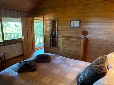A bedroom with a bed folded towels a dresser a mirror a door to a balcony and wooden walls at Treetops in Woody Bay