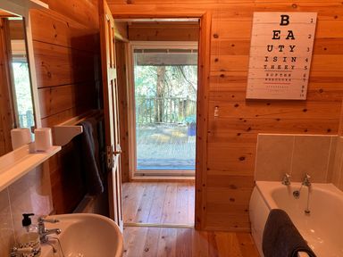 A wooden bathroom with a sink mirror towel rack bathtub and a doorway leading to a balcony at Treetops in Woody Bay