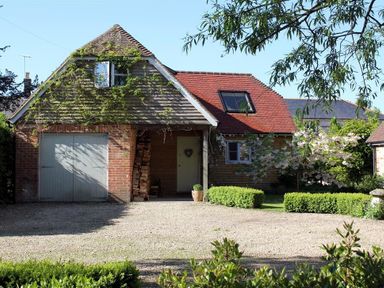 A house with a garage door surrounded by plants and trees at Bridge Studio in Broad Chalke