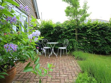 A patio with a white metal table and two chairs surrounded by plants and greenery at Bridge Studio in Broad Chalke