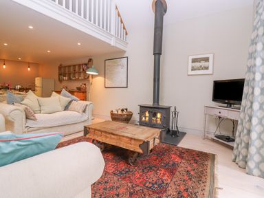 A living room with sofas a wooden coffee table a rug a wood stove and a television at Bridge Studio in Broad Chalke