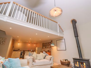 A living room with a wood stove and a staircase railing above at Bridge Studio in Broad Chalke