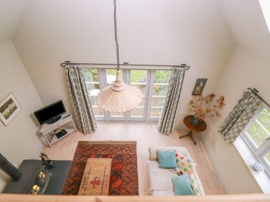 A living room with a sofa pillows television wood stove and a wooden table with a vase at Bridge Studio in Broad Chalke