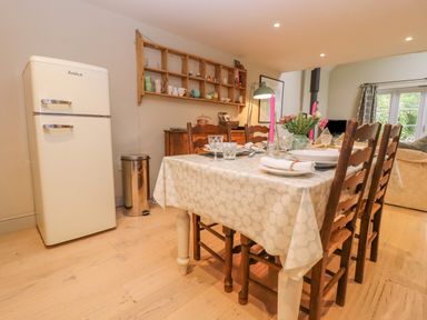 A dining area with a table set with plates and candles wooden chairs a refrigerator a shelf with mugs and a window at Bridge Studio in Broad Chalke
