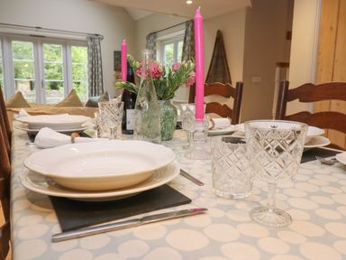 A dining table set with plates glasses pink candles and flowers at Bridge Studio in Broad Chalke