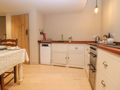 A kitchen with white cabinets a dishwasher a wooden door and a dining table with chairs at Bridge Studio in Broad Chalke