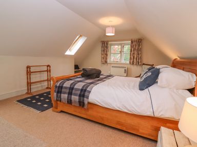 A bedroom with a wooden bed a window with curtains and a skylight at Bridge Studio in Broad Chalke