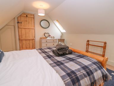 A bedroom with a wooden bed and plaid blanket near a wooden door and a dresser with a mirror at Bridge Studio in Broad Chalke