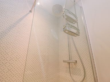 A shower area with patterned tiles a rain shower head and a wall-mounted shower shelf at Bridge Studio in Broad Chalke