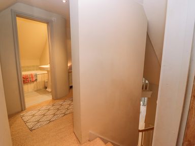 A hallway with carpeted stairs leading down and a doorway to a bathroom with a bathtub and sink at Bridge Studio in Broad Chalke