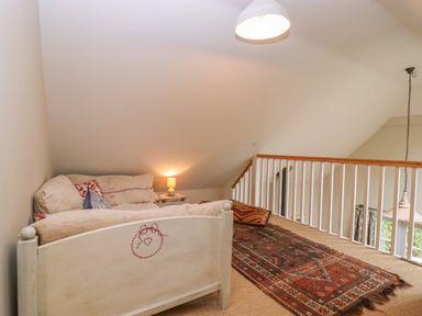 A loft area with a daybed, rug, lamp, and railing overlooking a window at Bridge Studio in Broad Chalke