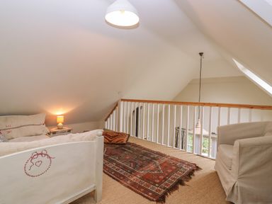 A loft area with a sofa, armchair, side table with lamp, and a patterned rug at Bridge Studio in Broad Chalke