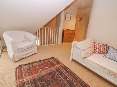 A seating area with a white armchair a wooden sofa with cushions a wooden cabinet and a patterned rug at Bridge Studio in Broad Chalke