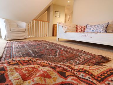 A sitting area with patterned rugs a white armchair and a white sofa with cushions at Bridge Studio in Broad Chalke