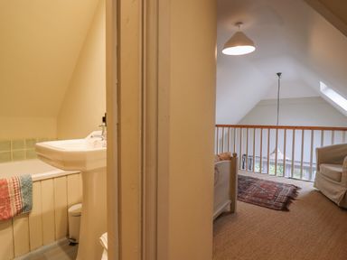 A bathroom with a sink and bathtub next to a living area with a chair and railing at Bridge Studio in Broad Chalke