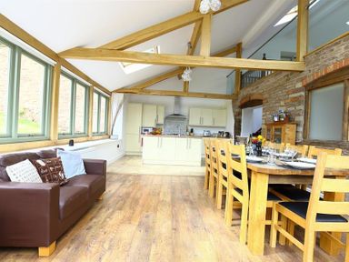 An open kitchen and dining area with wooden beams a brown sofa and large dining table at The Old Mill in Flaxley