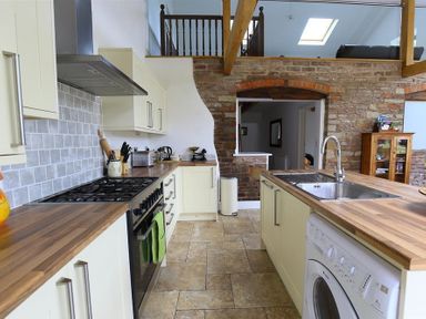 A kitchen with wooden countertops a sink a washing machine and built in stove beneath an open ceiling at The Old Mill in Flaxley