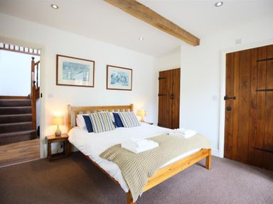 A bedroom with a wooden bed and side tables with lamps wooden doors and stairs visible at The Old Mill in Flaxley