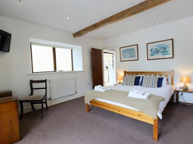 A bedroom with a wooden bed and towels on it two framed pictures on the wall and a chair near a window at The Old Mill in Flaxley