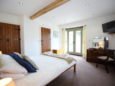 A bedroom with a bed pillows bedside lamps wooden doors dresser chair and glass doors at The Old Mill in Flaxley