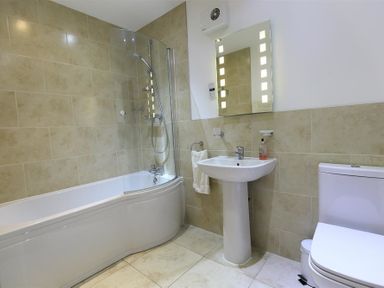 A bathroom with a bathtub and shower, sink with a mirror, and toilet at The Old Mill in Flaxley