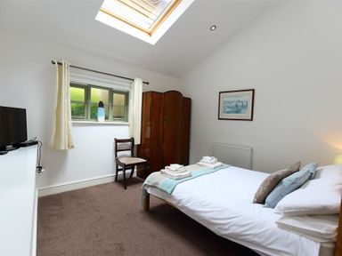 A bedroom with a double bed, wooden chair, wardrobe, window with curtains, and a skylight at The Old Mill in Flaxley