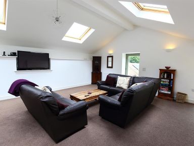 A living room with black leather sofas a wooden coffee table a television and skylights at The Old Mill in Flaxley