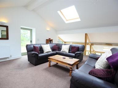 A living room with black leather sofas and a wooden coffee table under a skylight at The Old Mill in Flaxley