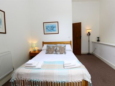 A bedroom with a bed a bedside table and lamp a wooden door and a floor lamp at The Old Mill in Flaxley