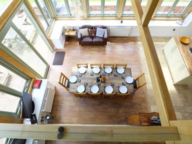 A dining area with a wooden table set for ten people a brown sofa and large windows at The Old Mill in Flaxley
