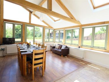 A dining room with a wooden table set for twelve and a sofa by windows at The Old Mill in Flaxley