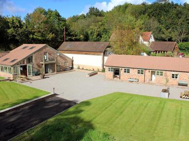 A courtyard with stone buildings surrounded by grass and trees at The Old Mill in Flaxley