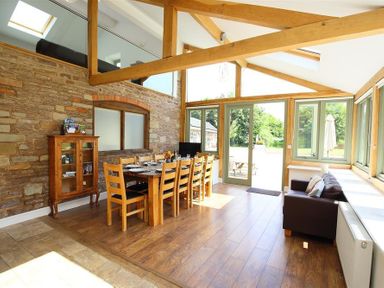 A dining area with a wooden table set for eight and a small sofa near large windows at The Old Mill in Flaxley
