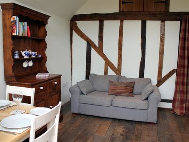 A room with a gray sofa, wooden cabinet with blue and white tea set, and a dining table with white chairs at Pop's Barn in Downton
