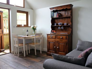 A dining area with a wooden table and two chairs next to a wooden cupboard and a gray sofa at Pops Barn in Downton