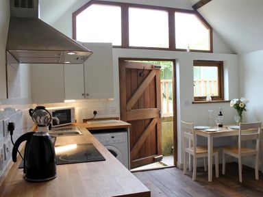 A kitchen with wooden countertop a kettle microwave stove and a dining table with chairs near a wooden door at Pops Barn in Downton