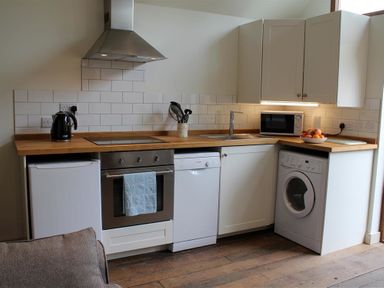 A kitchen with wooden countertops white cabinets a stove a dishwasher a washing machine a microwave and a kettle at Pops Barn in Downton