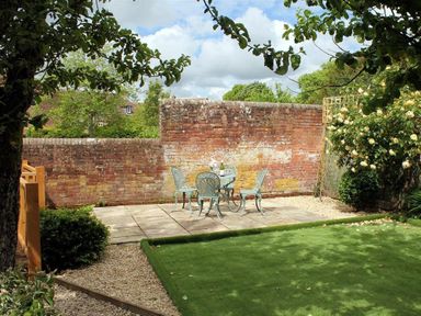 A garden with a paved patio area with a table and four chairs set against a brick wall at Pops Barn in Downton