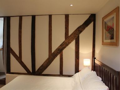 A bedroom with wooden beam accents on the wall a bed with white bedding a bedside lamp and a framed picture at Pop's Barn in Downton