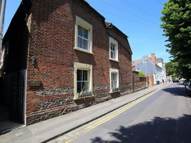 A brick building with four windows along a street with parked cars and trees at Rojoy in Salisbury