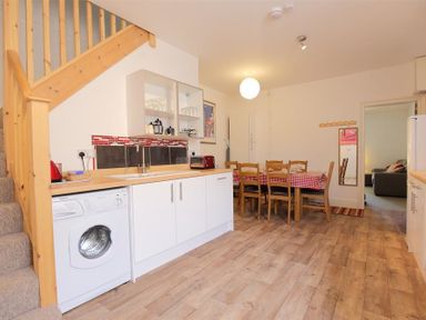 A kitchen with white cabinets washing machine and wooden stairs next to a dining area with a red checked tablecloth at Rojoy in Salisbury