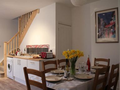 A dining table set with plates glasses and a vase of yellow flowers near a small kitchen under wooden stairs at Rojoy in Salisbury